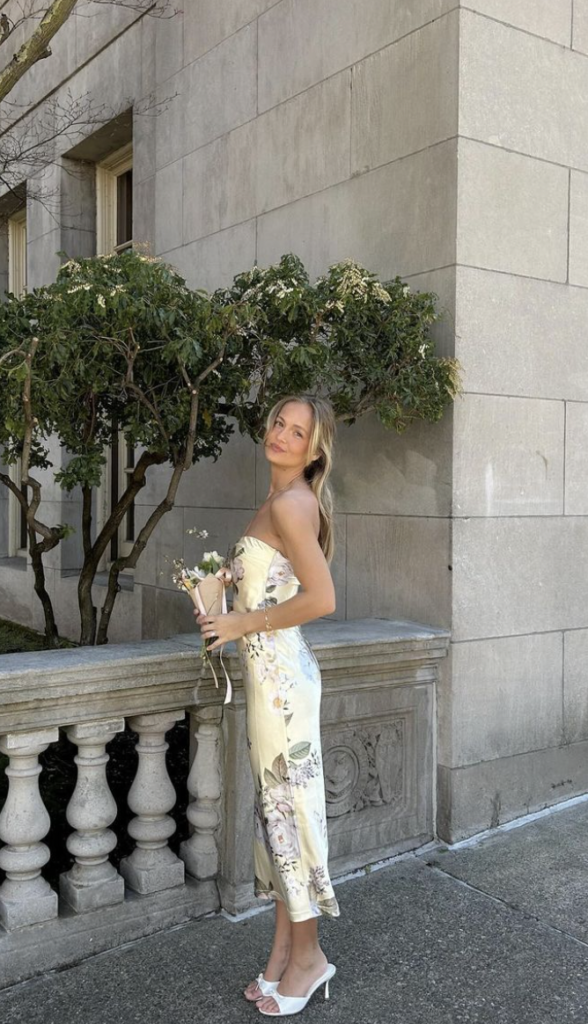 Woman standing outside in a floral dress holding flowers.